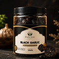 A jar of Panchal Organic Black Garlic, 1000g, on a dark textured surface with whole and sliced garlic cloves and green foliage in the background.