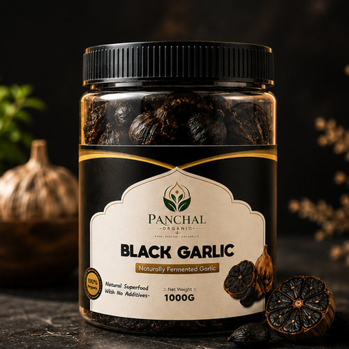 A jar of Panchal Organic Black Garlic, 1000g, on a dark textured surface with whole and sliced garlic cloves and green foliage in the background.